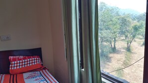 A room with a bed, a window with curtains, and a view of trees outside. - Hotel Thamsar (Palampur)