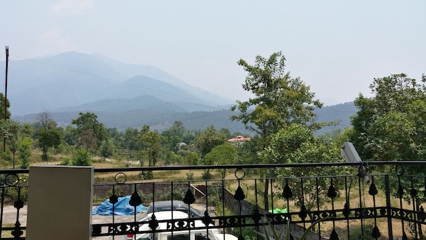 A balcony with a view of a mountainous landscape, a parked car, and a metal fence. - Hotel Thamsar (Palampur)