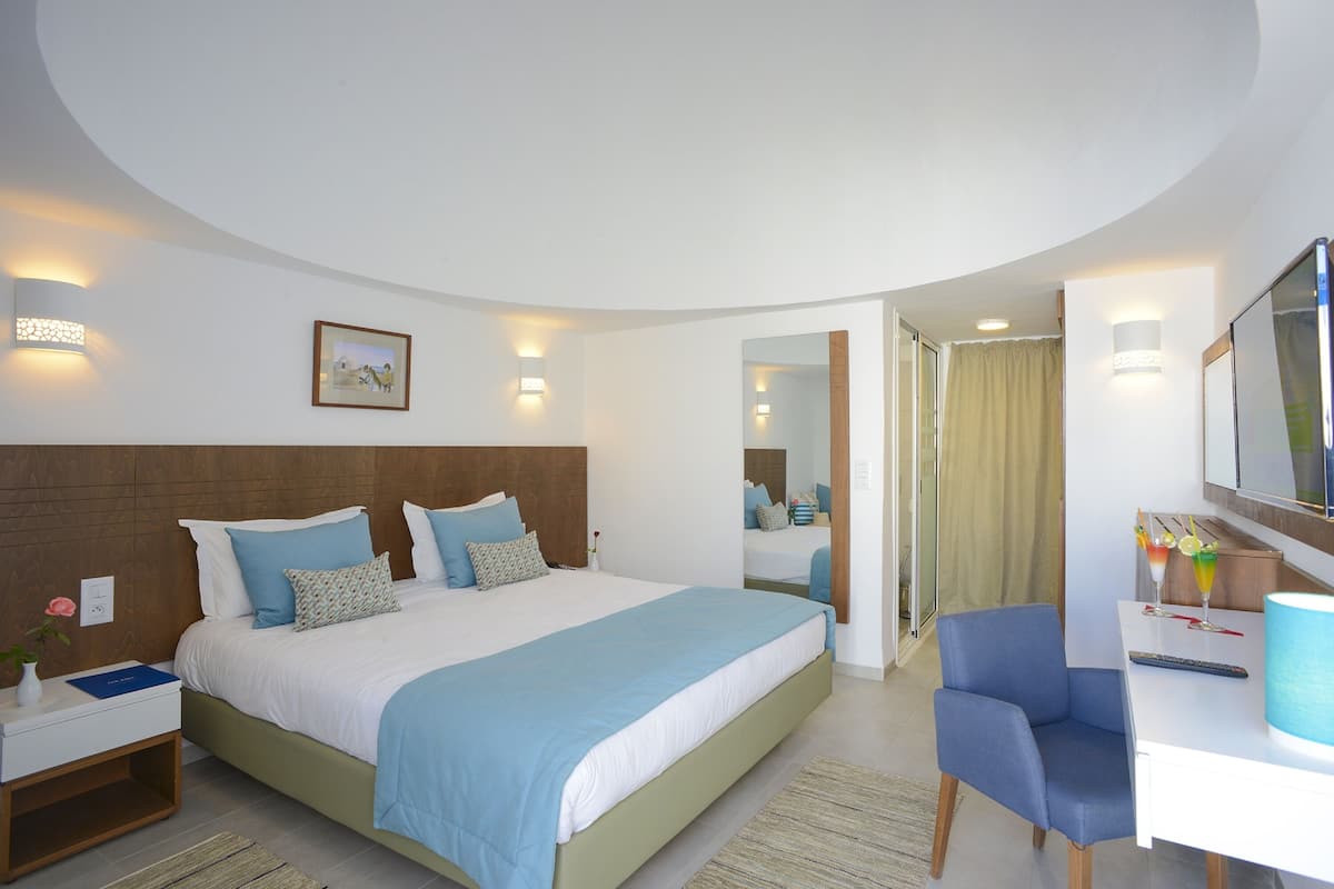 A modern hotel room with a large bed, a desk with a chair, a TV, and a bathroom visible through an open door.