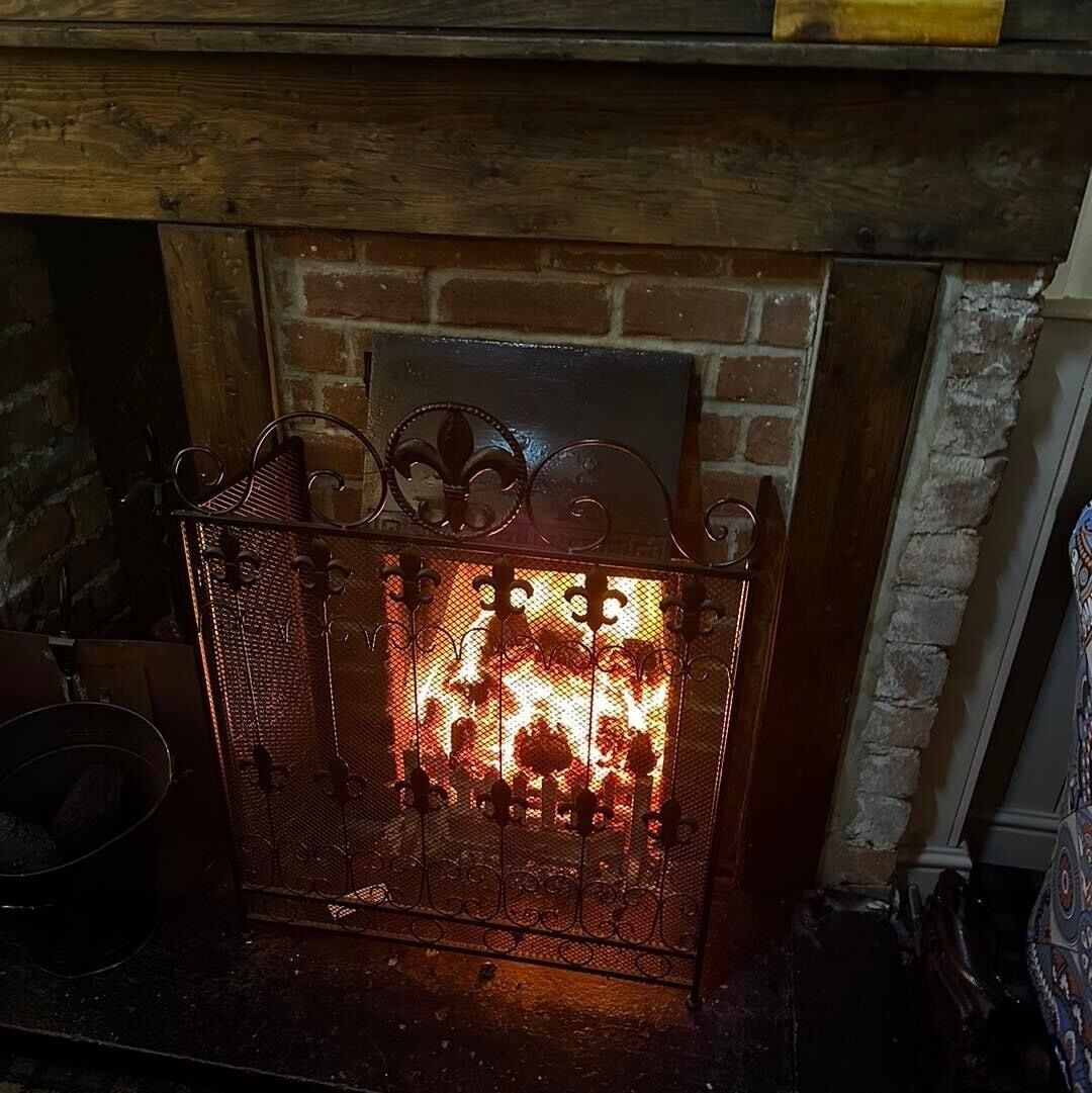 Una chimenea con una protección metálica y un muro de ladrillo al fondo.
