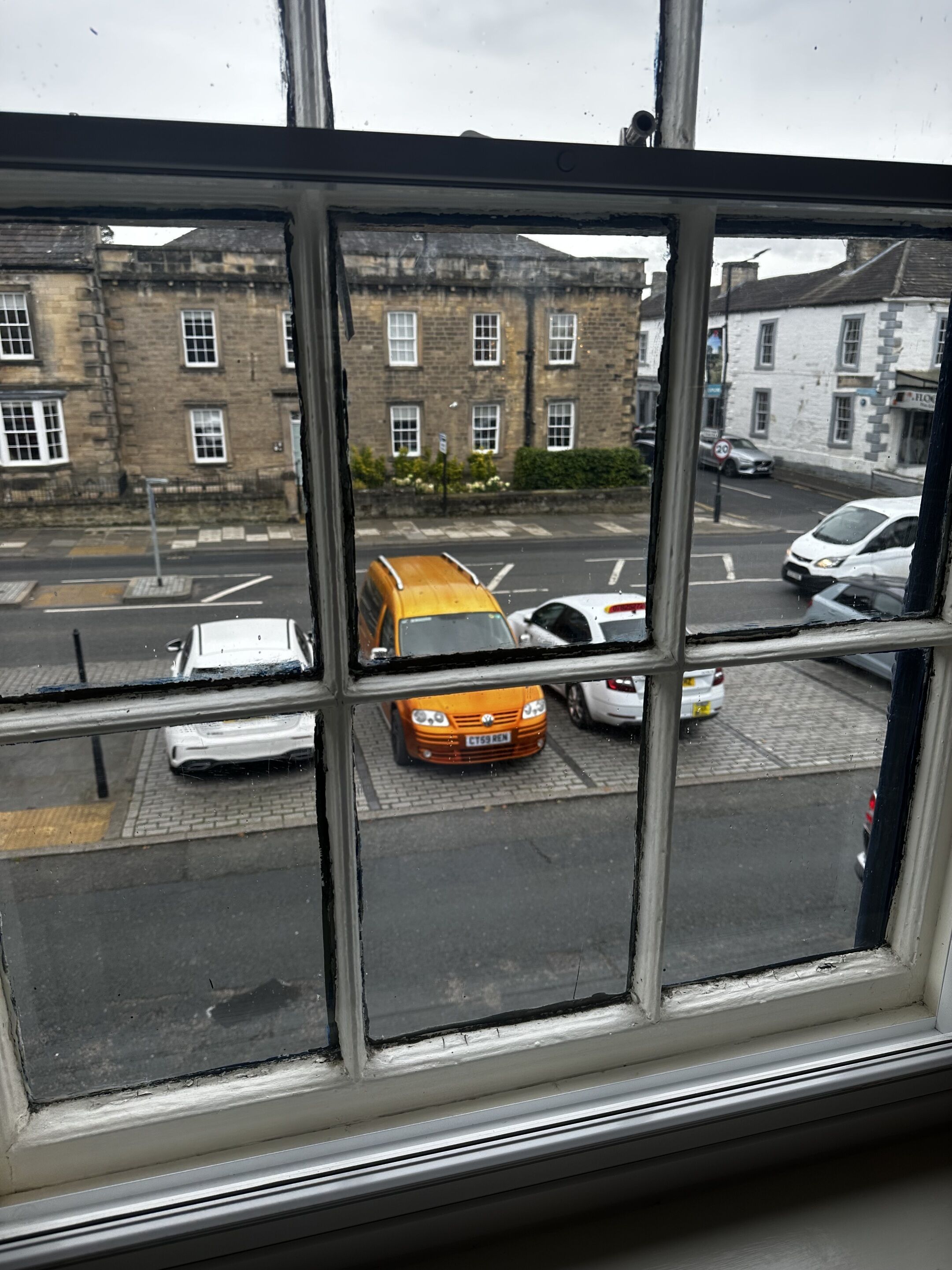 A view through a window of a street with parked cars and buildings in the background.