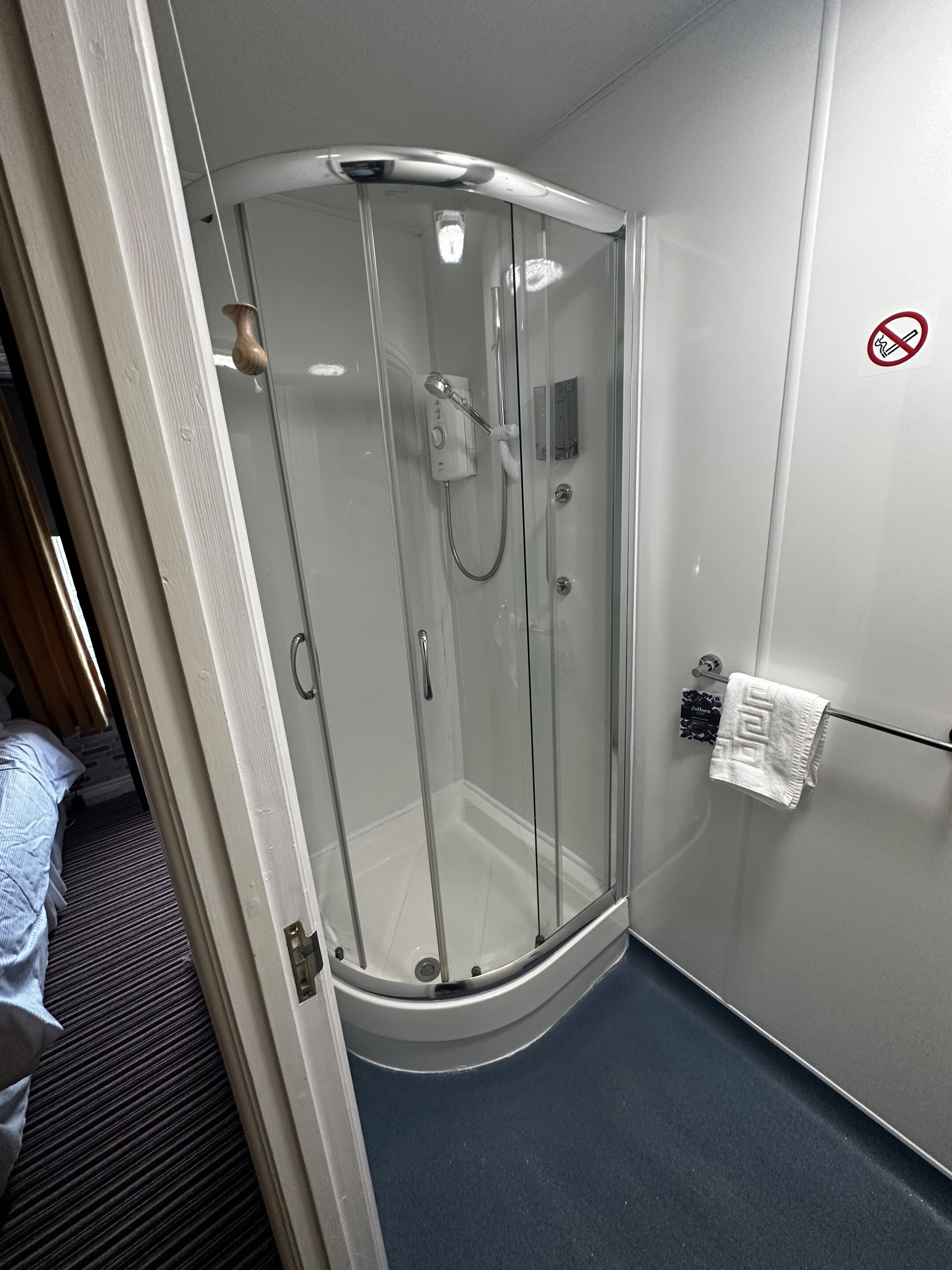A glass-enclosed shower stall with a control panel, a towel rack with a white towel, and a no-smoking sign on the wall.