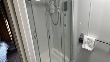 A glass-enclosed shower stall with a control panel, a towel rack with a white towel, and a no-smoking sign on the wall.