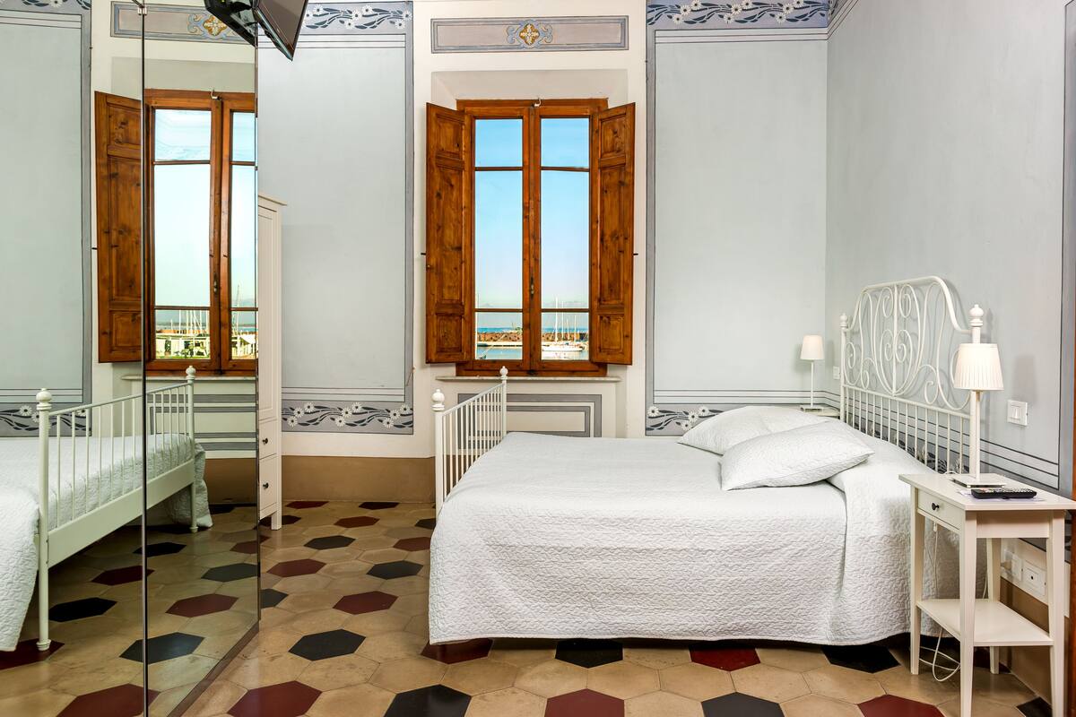 A bedroom with a bed, a nightstand, a desk, and a window with wooden shutters.