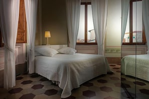 Un dormitorio con cama, mesita de noche, lámpara y ventana con cortinas.