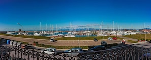 Un puerto deportivo con barcos amarrados, un área de estacionamiento con coches, y un cielo azul despejado.