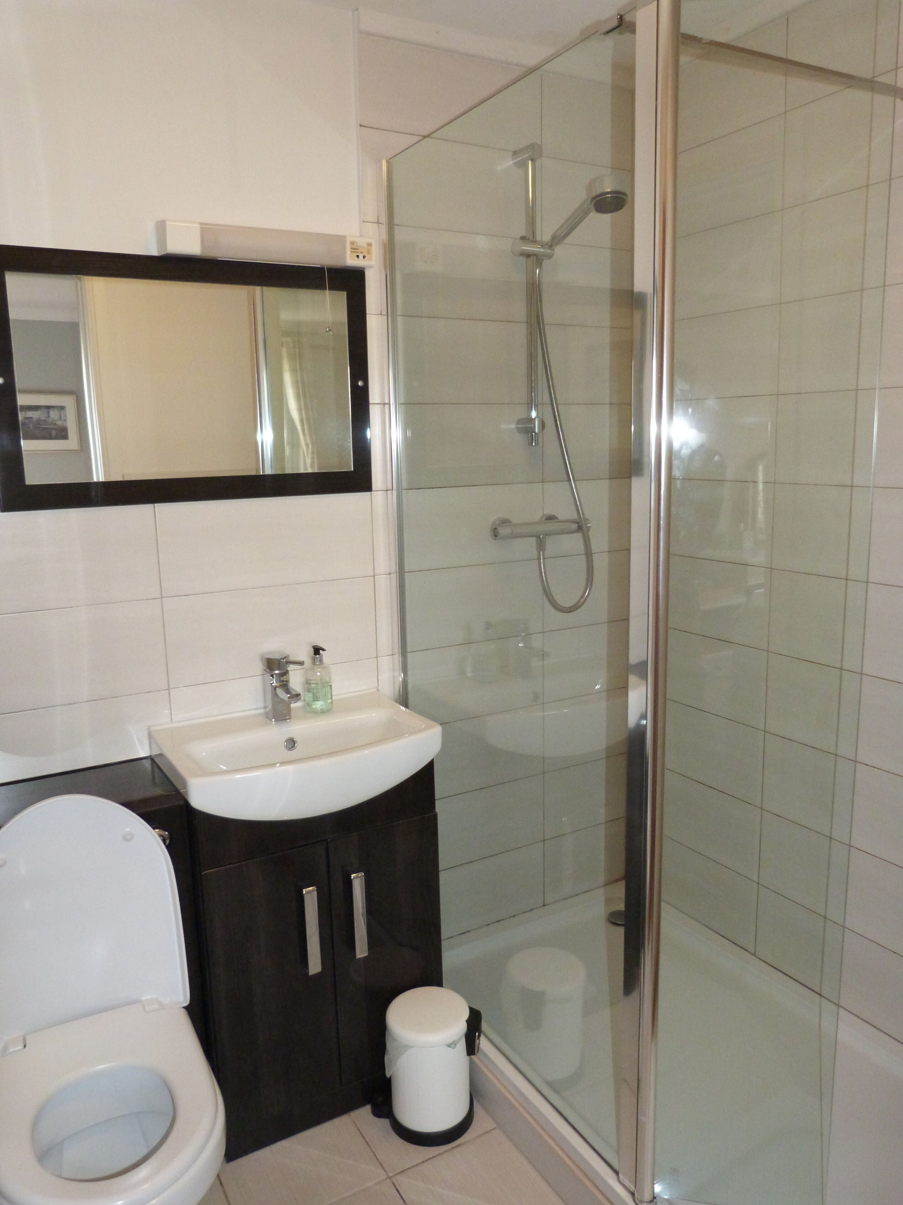 A bathroom with a toilet, sink, mirror, and glass-enclosed shower.