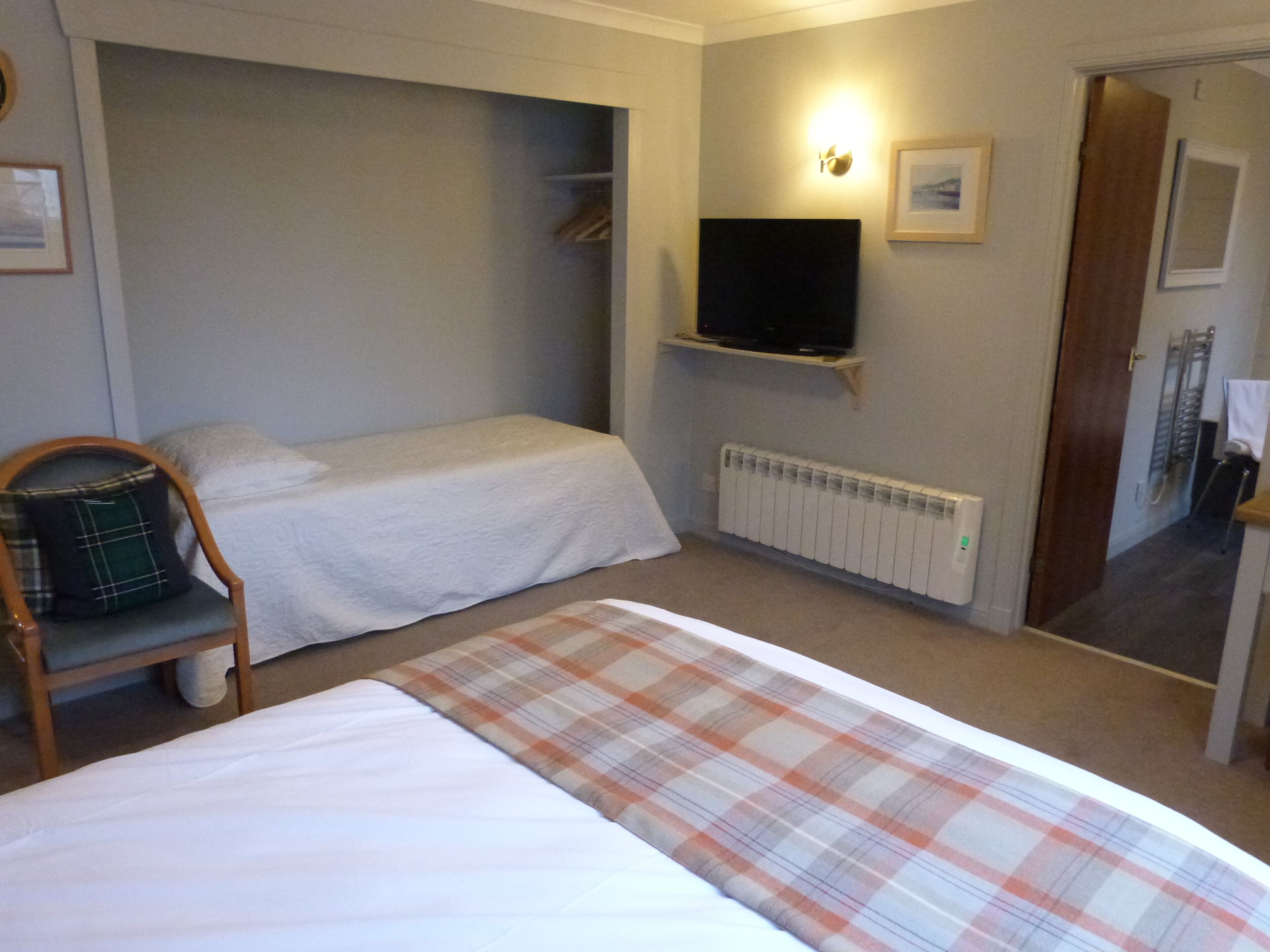 A bedroom with a bed, a chair, a television, a radiator, and a door.