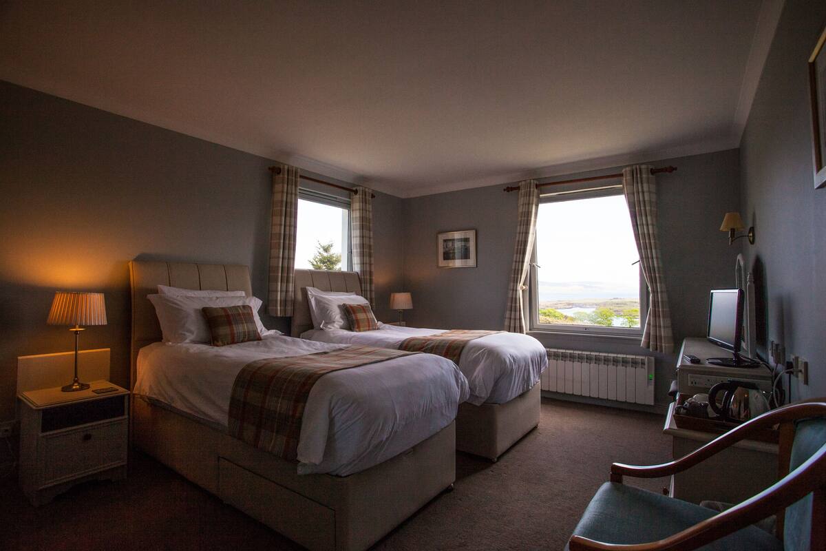 A hotel room with two beds, a desk with a computer, a chair, and a view of the outdoors.