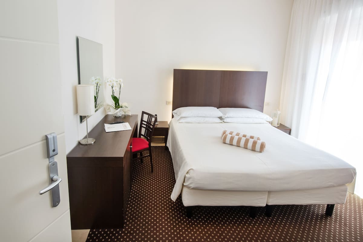 Une chambre d’hôtel comprenant un lit, un bureau avec une chaise, un miroir et une table de chevet.