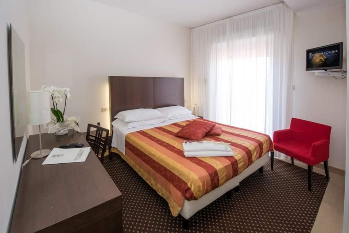 Une chambre d’hôtel équipée d’un lit, d’un bureau, d’une chaise, d’une télévision et d’une fenêtre avec des rideaux.