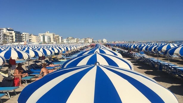 A beach with rows of blue and white striped umbrellas and lounge chairs.