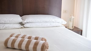 A neatly made bed with white linens and a striped towel, a wooden headboard, and a bedside table with a white lamp.