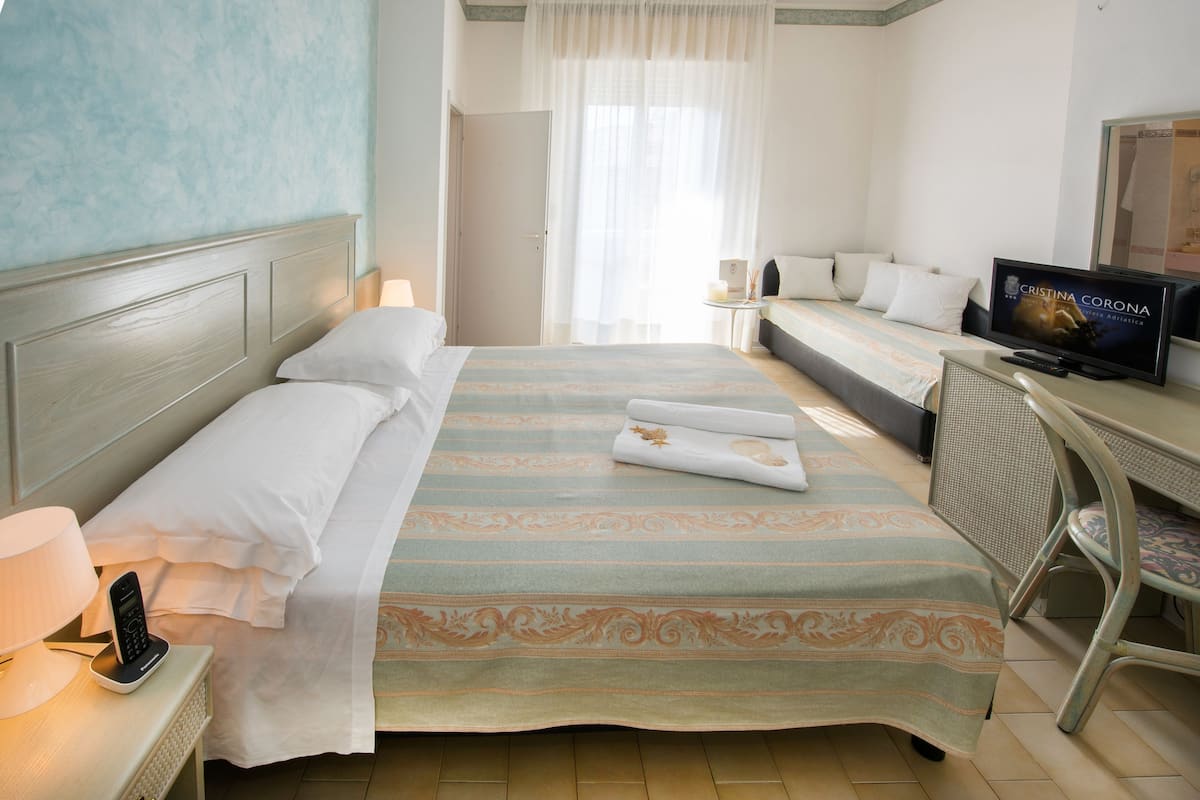 Une chambre d’hôtel comprenant un lit, un bureau avec une télévision, une chaise et une table de chevet avec une lampe et un tél éphone.