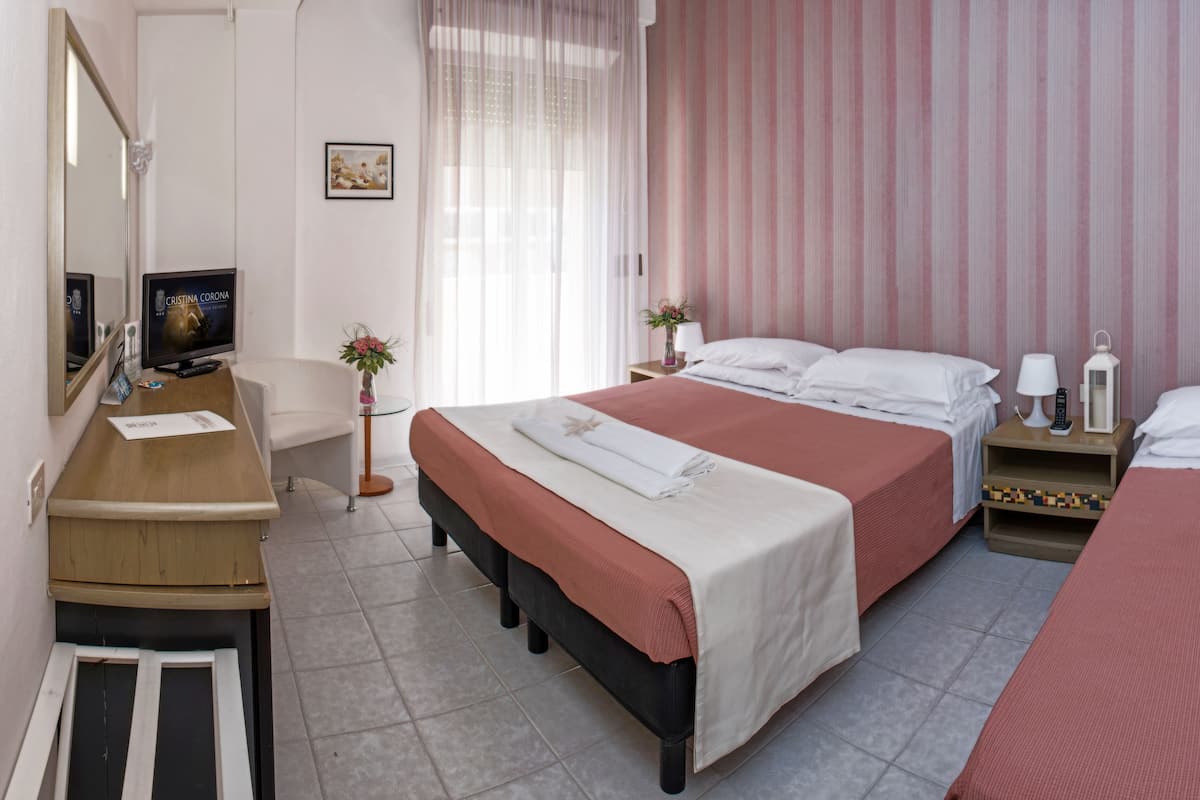 Une chambre d’hôtel avec deux lits, un bureau, une chaise, une télévision et une fenêtre avec des rideaux.