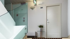 A modern hotel lobby with a glass staircase, a reception desk, and a closed door.