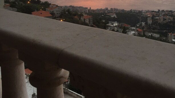 A balcony overlooking a cityscape with a sunset view over the sea. - Nice view Apartment (Chnaneir)