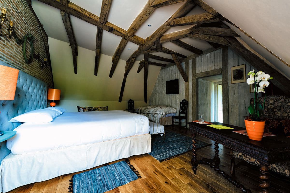 A bedroom with a bed, wooden beams, a brick wall, and a window.