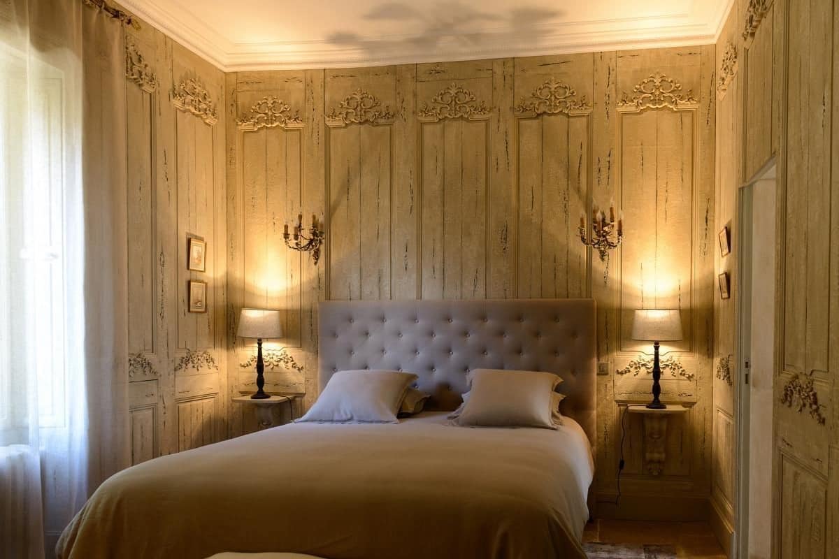 A bedroom with a large bed, two bedside tables with lamps, and ornate wall paneling.