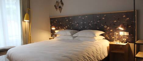 Una cama bien hecha con sábanas blancas, una lámpara de noche, un reloj y un cabecero estampado con motivos florales.