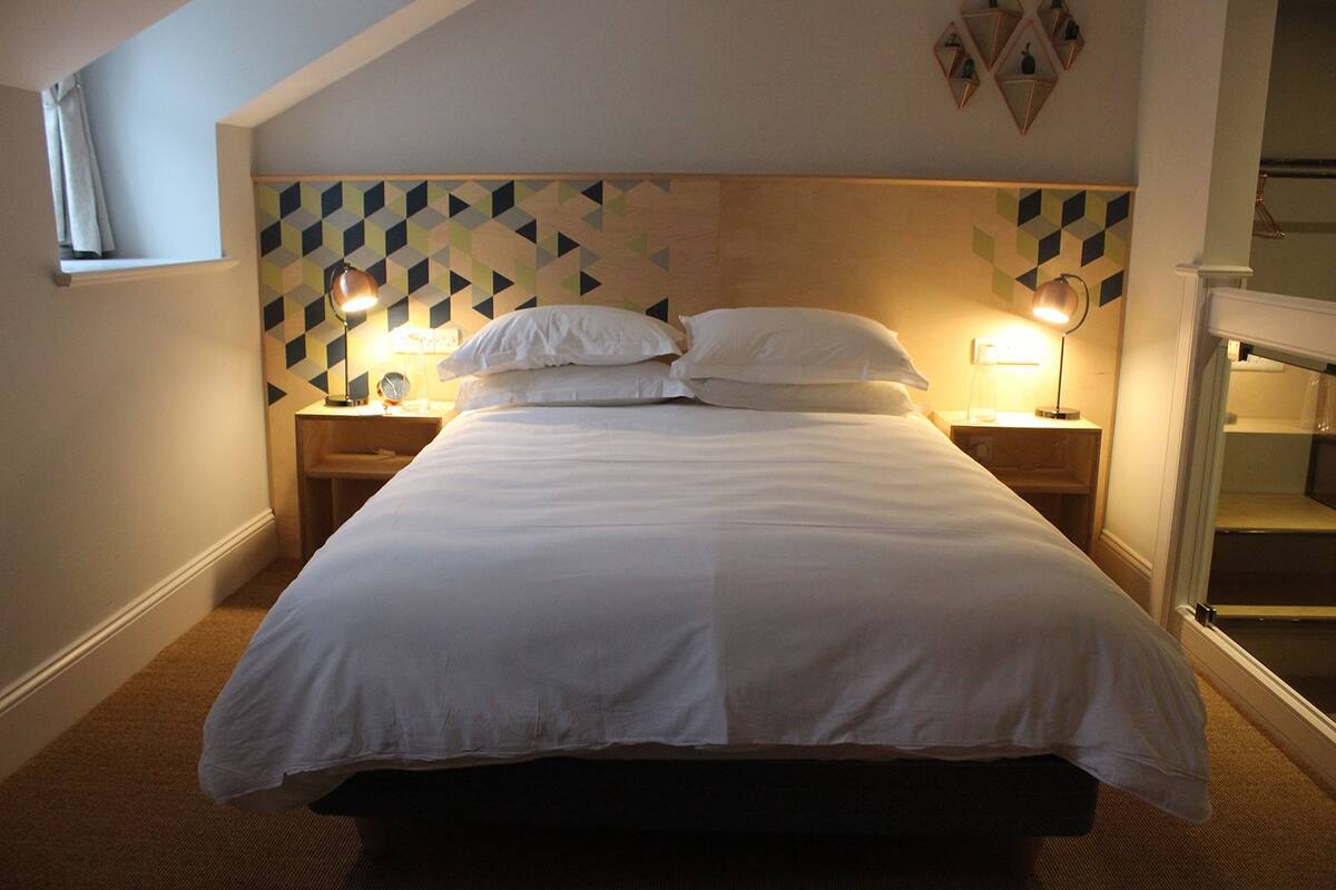 A neatly made bed with white linens, two bedside lamps, and a geometric-patterned headboard.