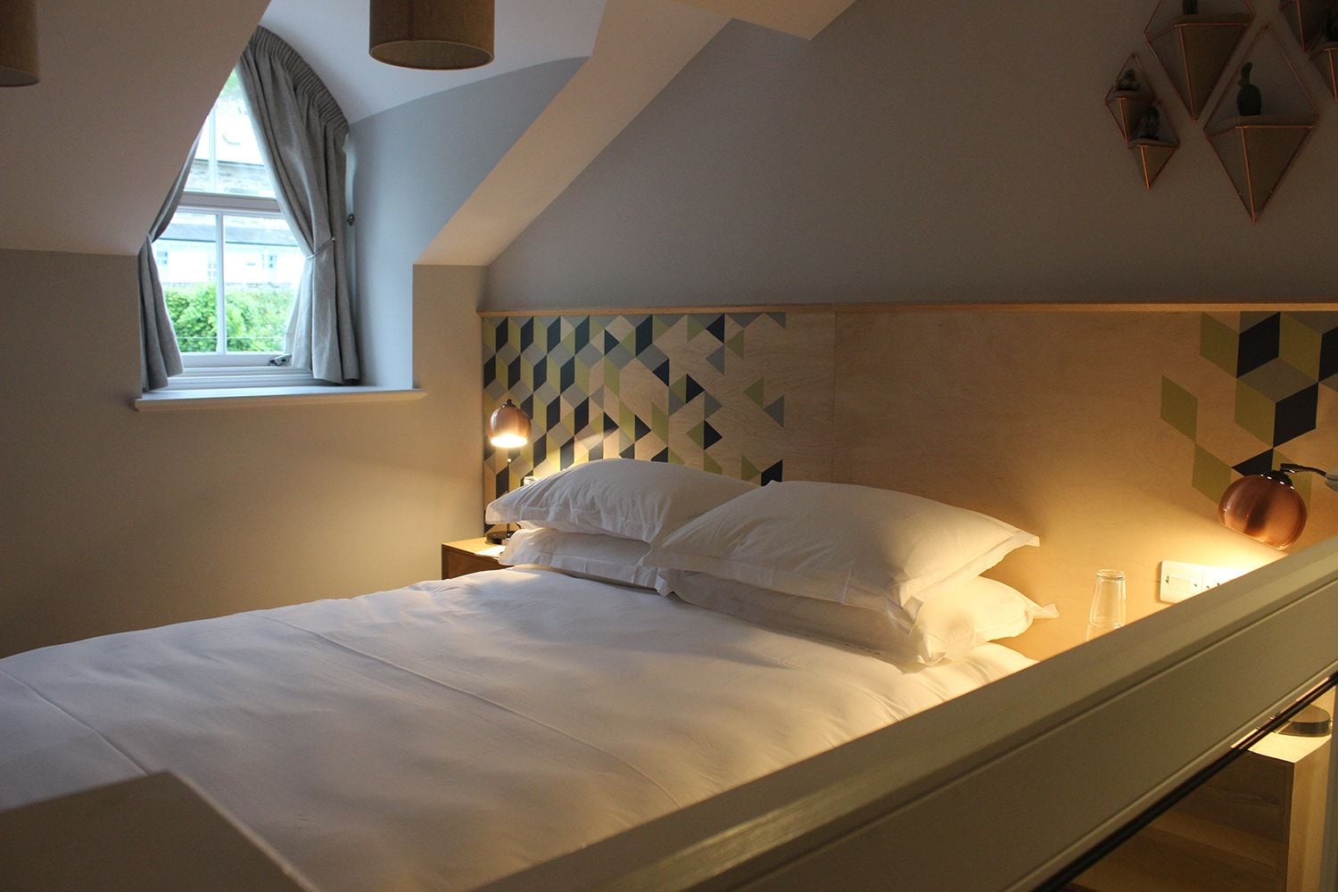 A bedroom with a bed, a window with curtains, and a geometric-patterned wall.