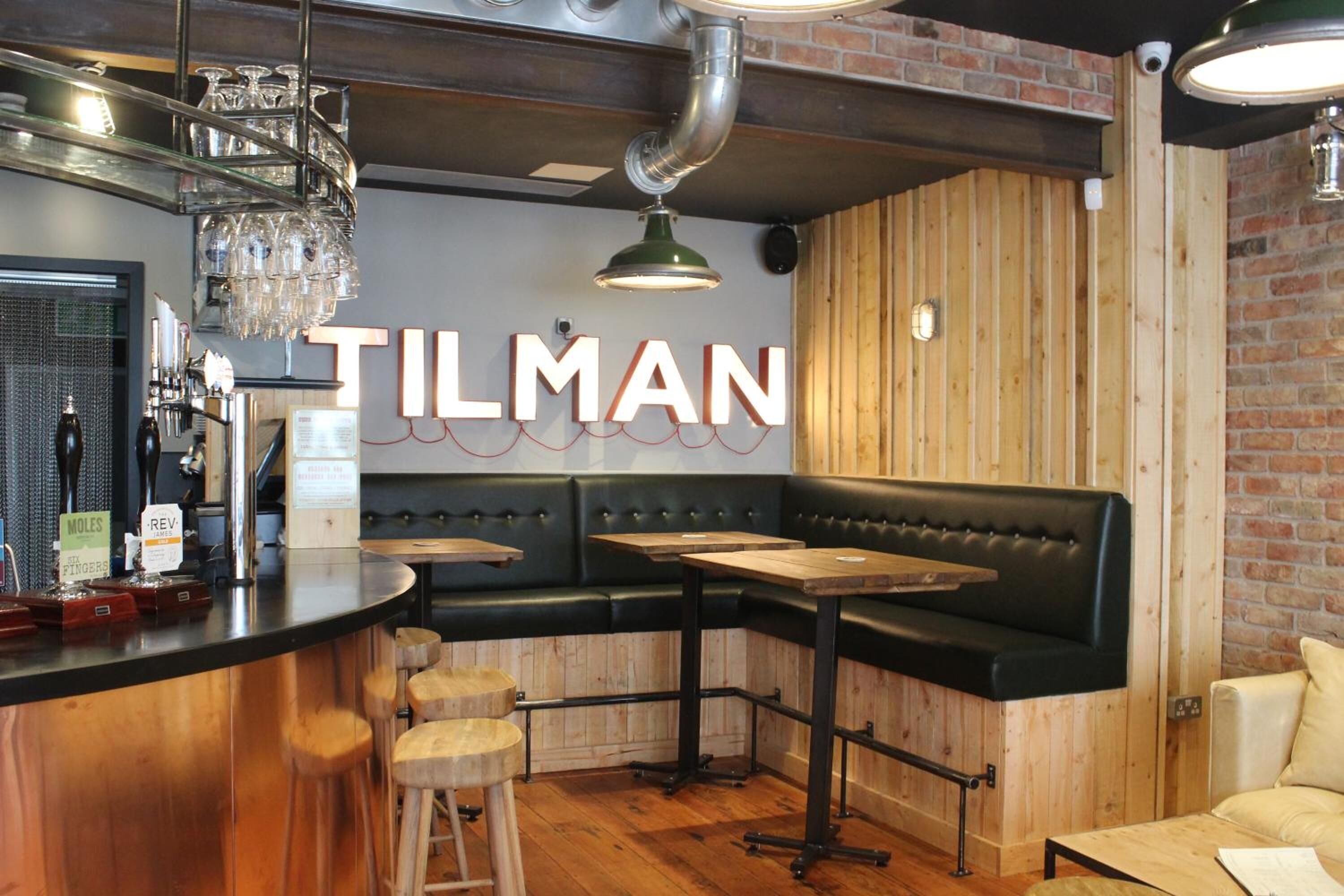 L’intérieur d’un restaurant avec un bar, des tables en bois, un coin salon avec des banquettes en cuir noir et un mur en briques.