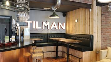 L’intérieur d’un restaurant avec un bar, des tables en bois, un coin salon avec des banquettes en cuir noir et un mur en briques.