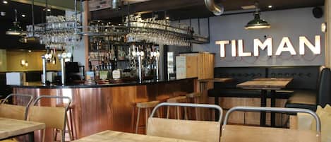Interior de un restaurante con barra, mesas y sillas de madera.