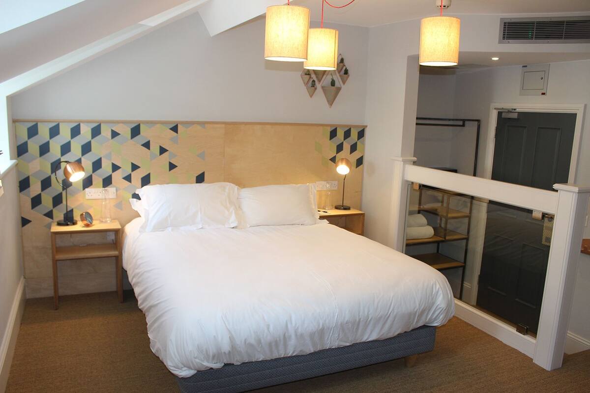 A bedroom with a bed, nightstands, lamps, and a geometric-patterned wall.