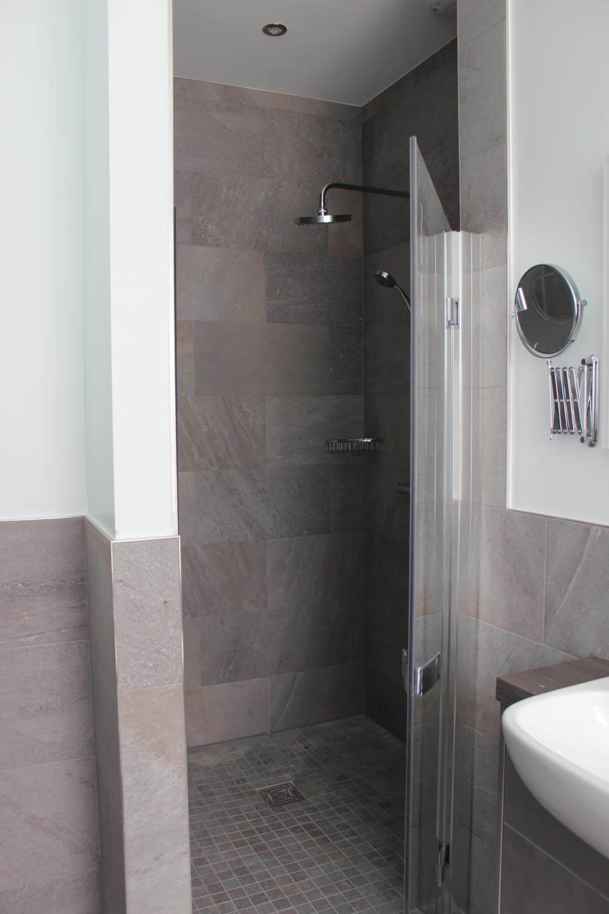 A modern bathroom with a glass-enclosed shower, a white sink, and a mirror with towel racks.