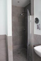 Un baño moderno con ducha de vidrio, un lavamanos blanco y un espejo con toalleros.