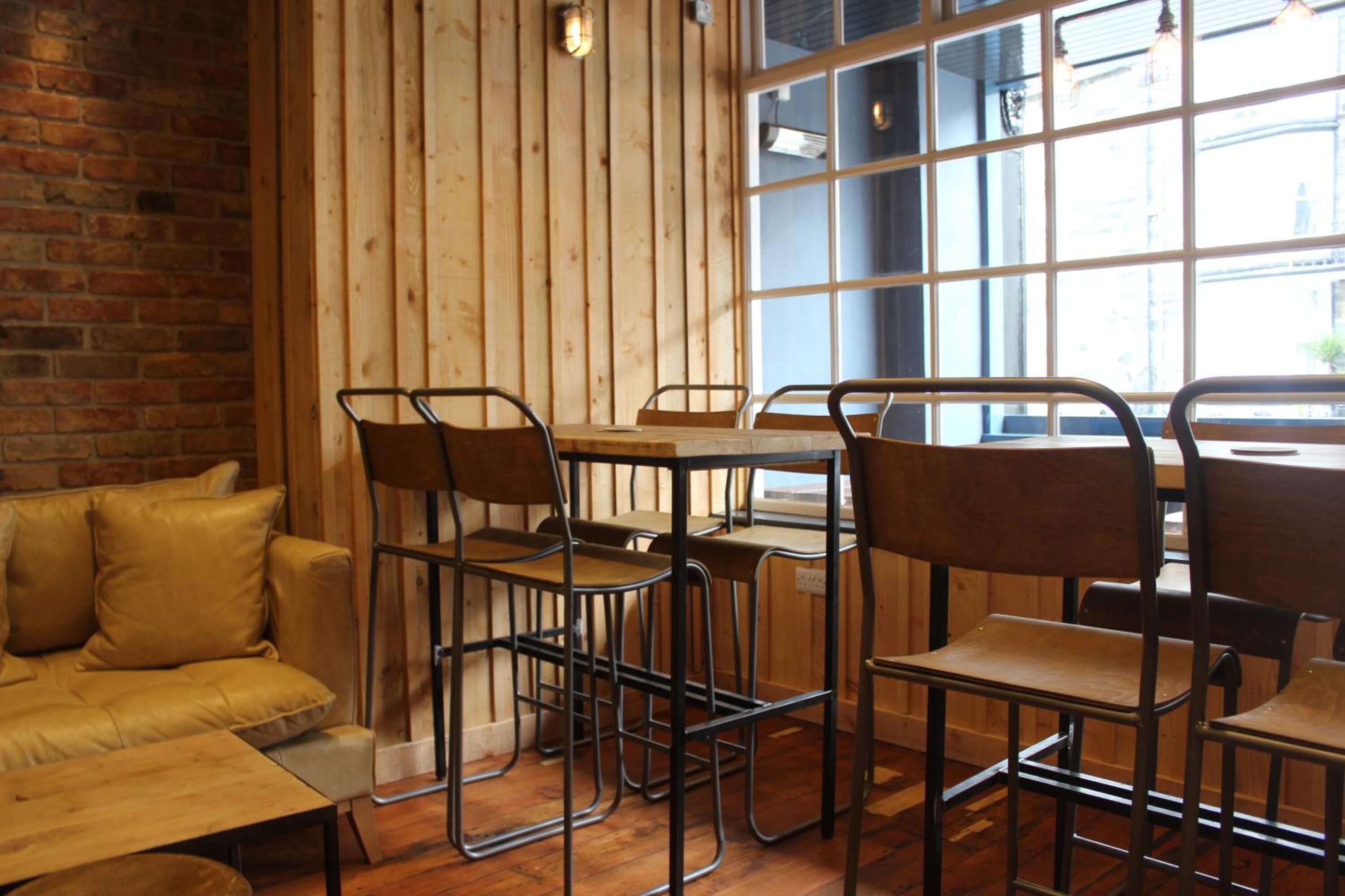 A cozy restaurant interior with wooden walls, a brick accent wall, and a large window providing natural light.