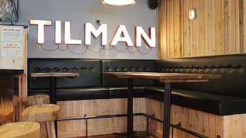 Interno di un ristorante con parete in legno, una panca in pelle nera e un cartello con la scritta "TILMAN".