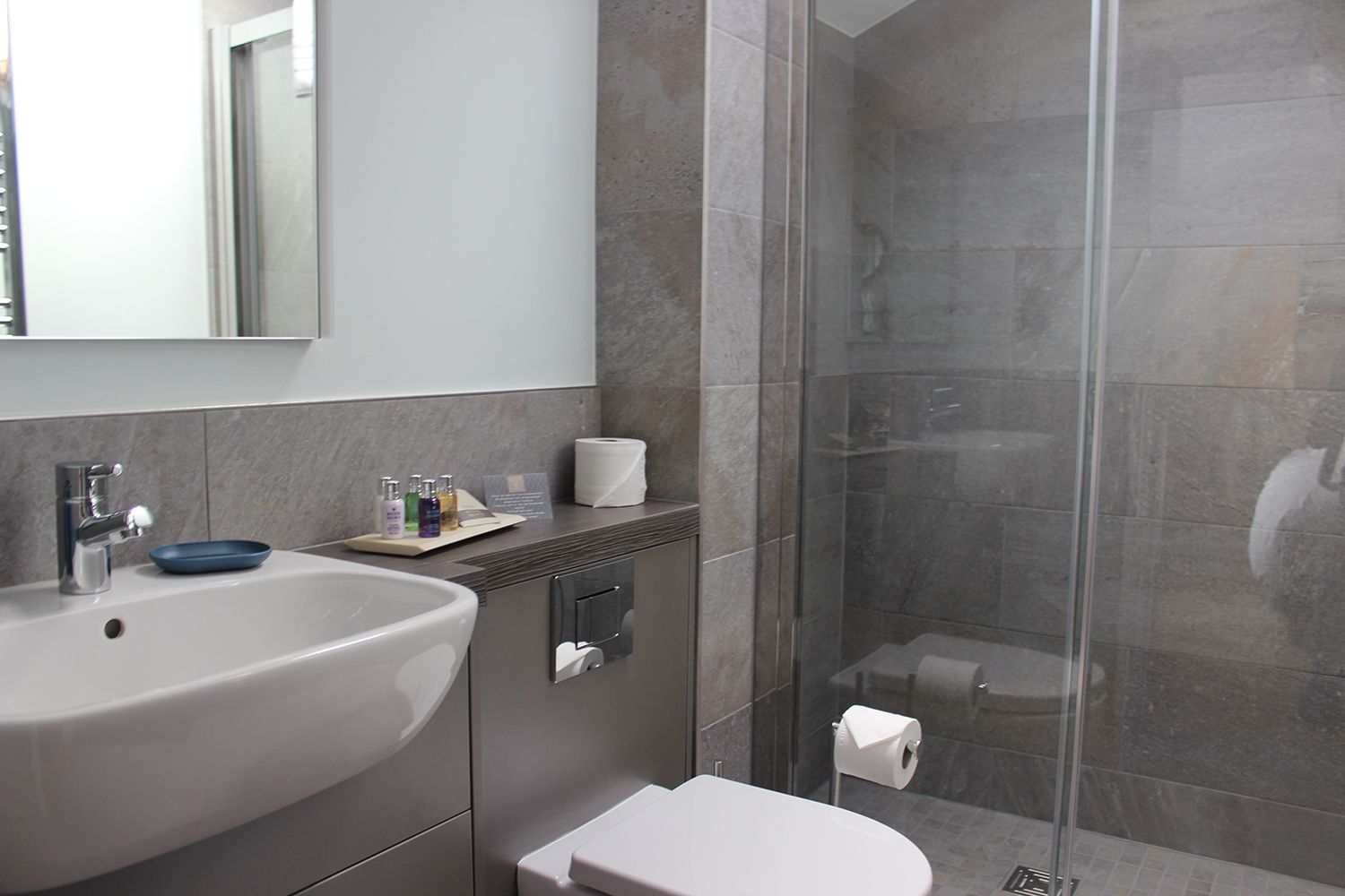 A modern bathroom with a large sink, mirror, and glass shower enclosure.