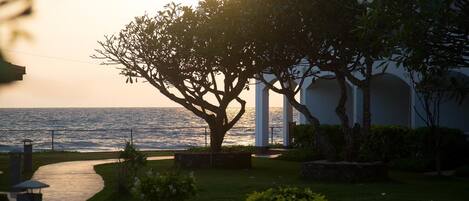 Una propiedad costera con un camino que lleva a un edificio blanco con columnas, rodeada de vegetación y con vistas al mar.