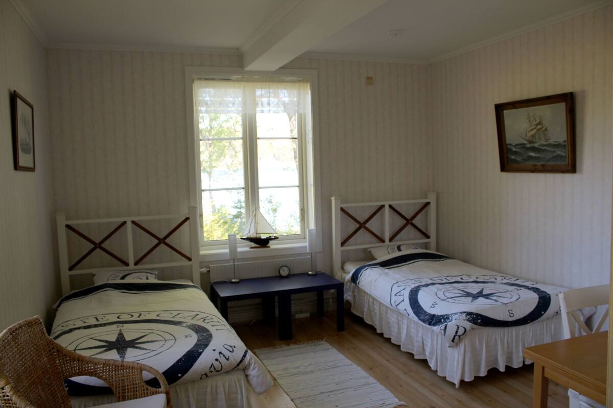 A room with two beds, a window, a table, and a chair.