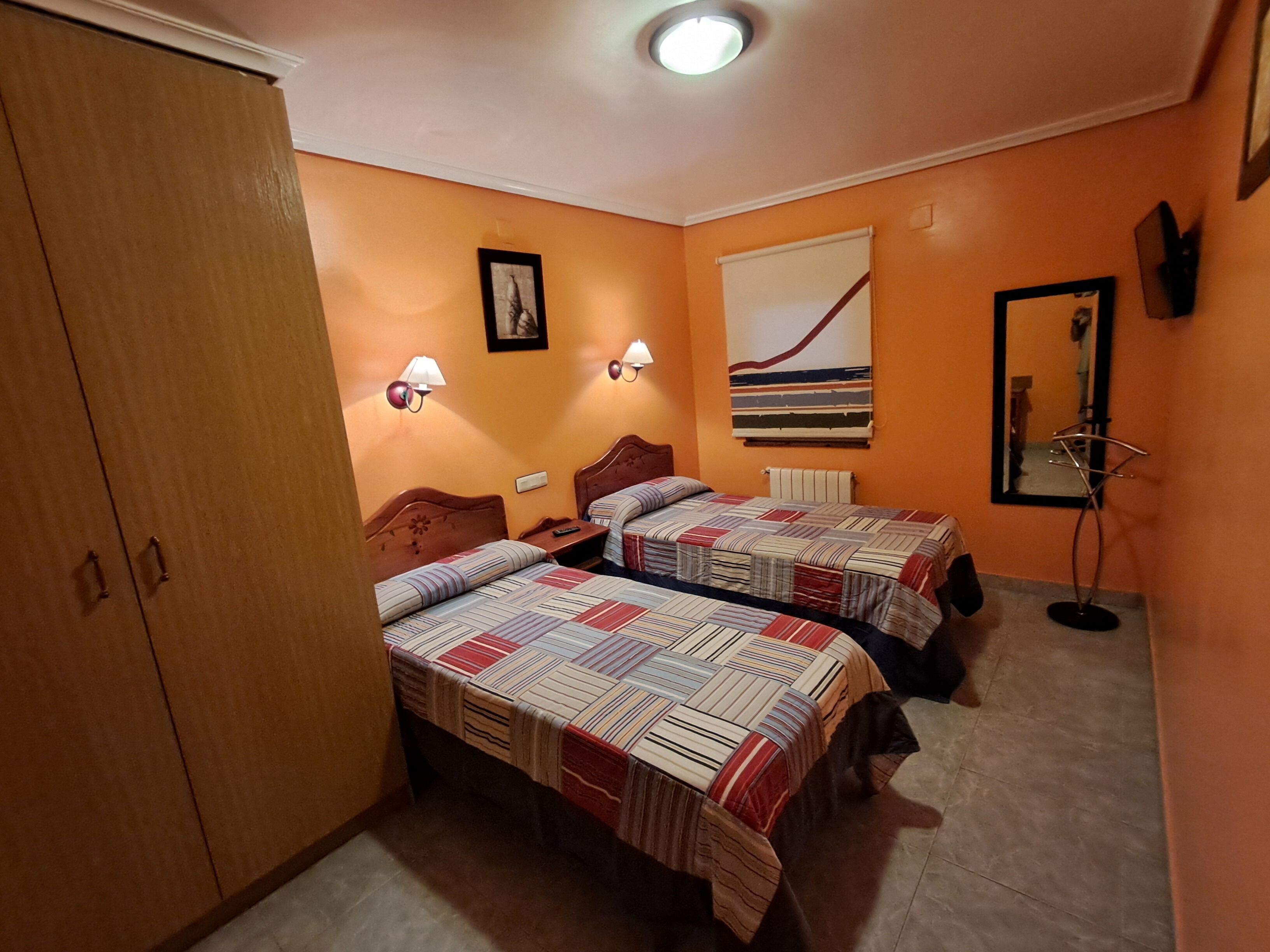 A hotel room with two beds, a wardrobe, a mirror, and a wall with a striped artwork.