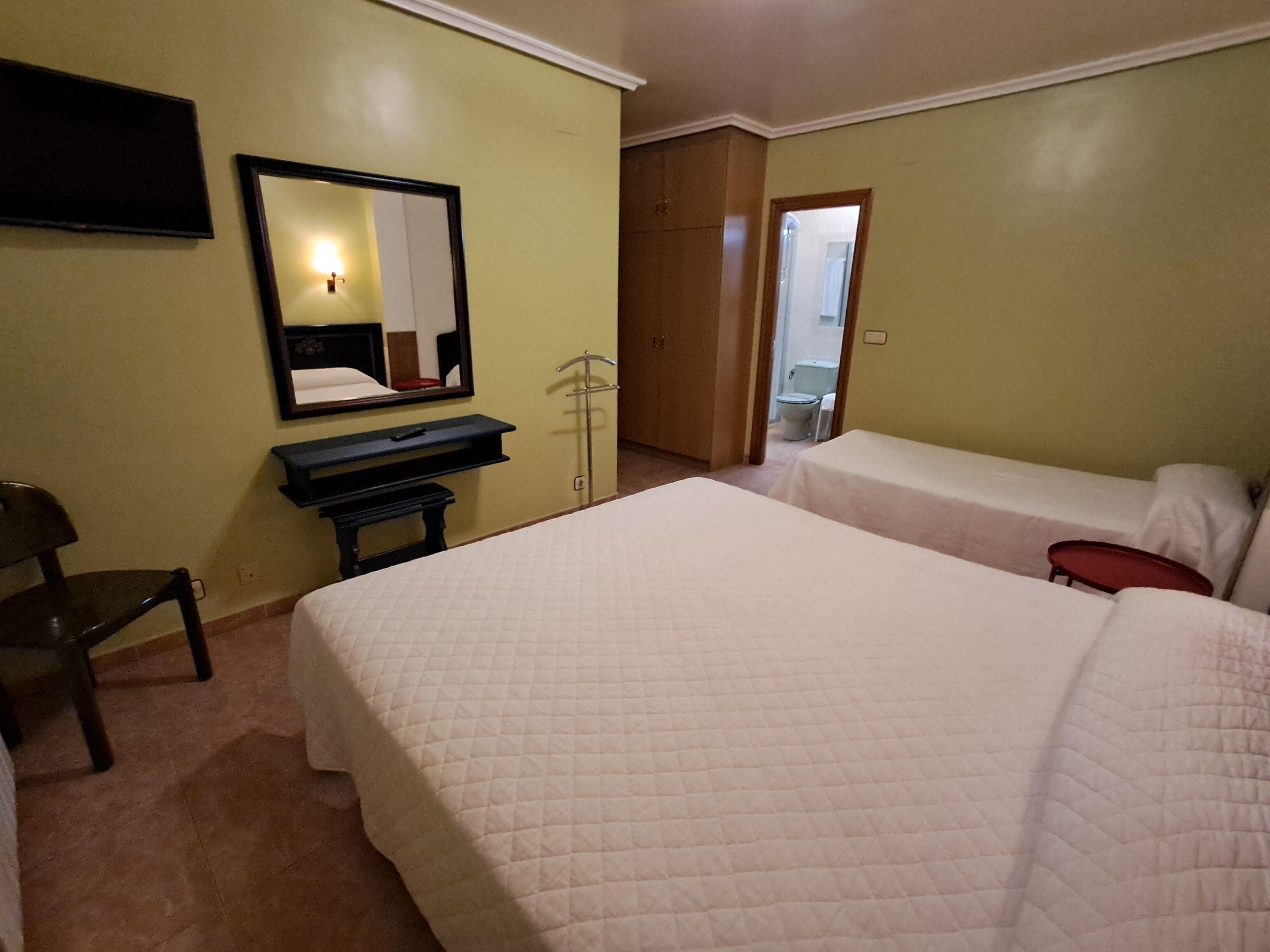 A hotel room with two beds, a desk, a chair, a TV, and a mirror.