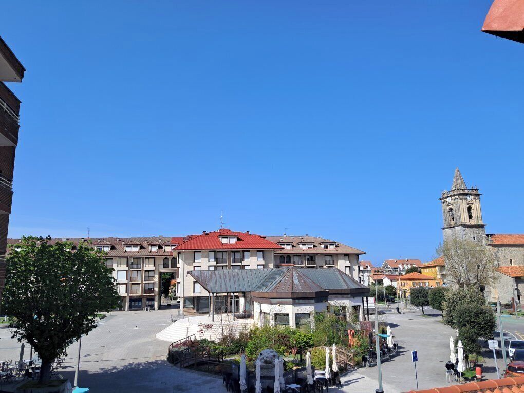 A plaza with a gazebo, a clock tower, and multi-story buildings with red roofs.