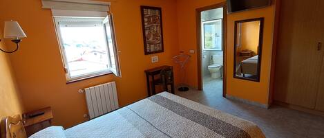 Une chambre à coucher comprenant un lit, un radiateur, une fenêtre, une porte donnant sur une salle de bain et un miroir.