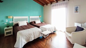 A hotel room with two beds, a ceiling fan, a window with curtains, a white chair, and a small table. - Casa Rural La Covacha (Losar de la Vera)