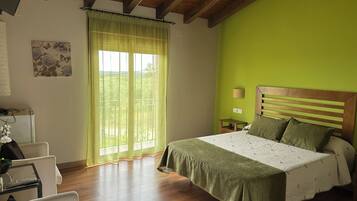 Un dormitorio con techo de madera, una cama con cubrecama verde, una mesita de noche con una lámpara y una ventana con cortinas traslúcidas.