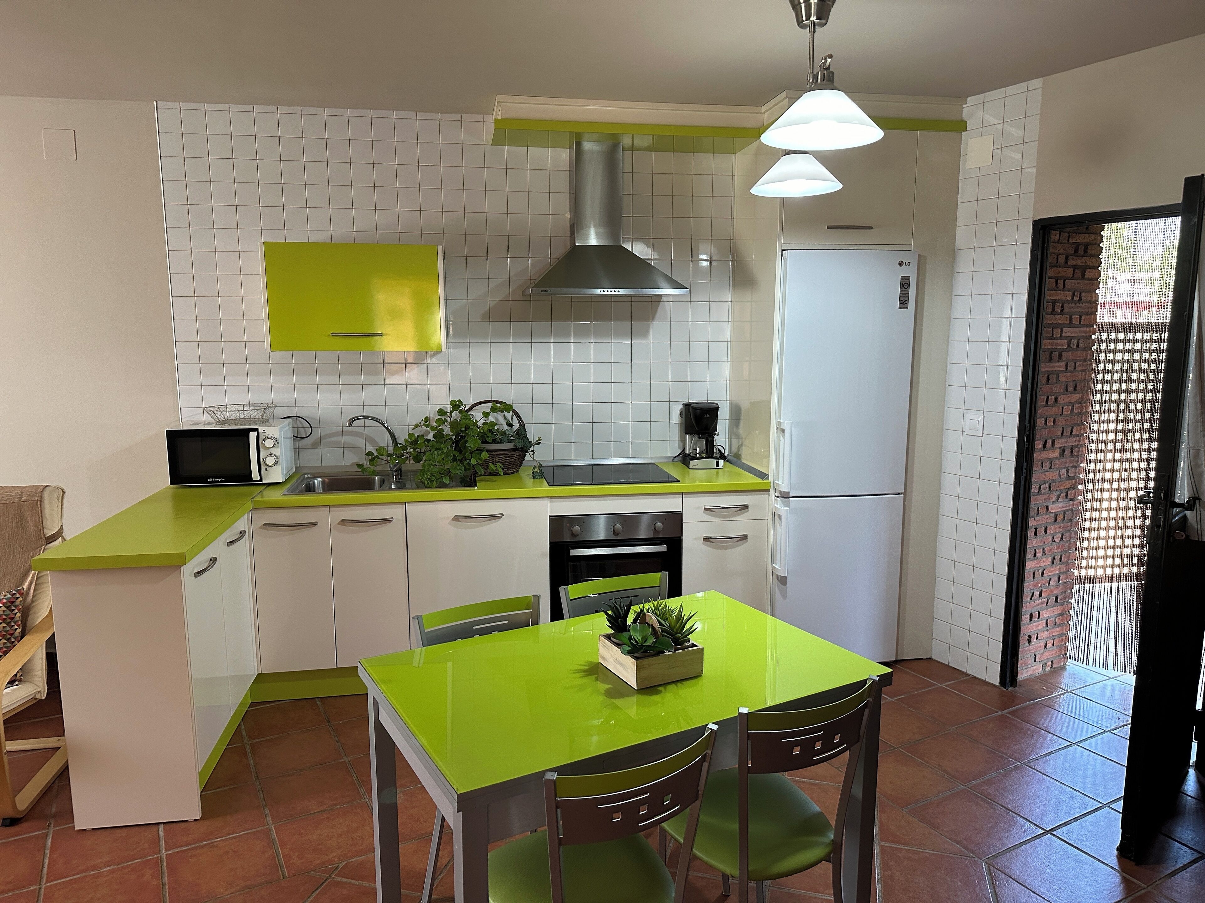 A compact kitchen with white cabinets, a green countertop, a microwave, a sink, a stove, and a refrigerator.