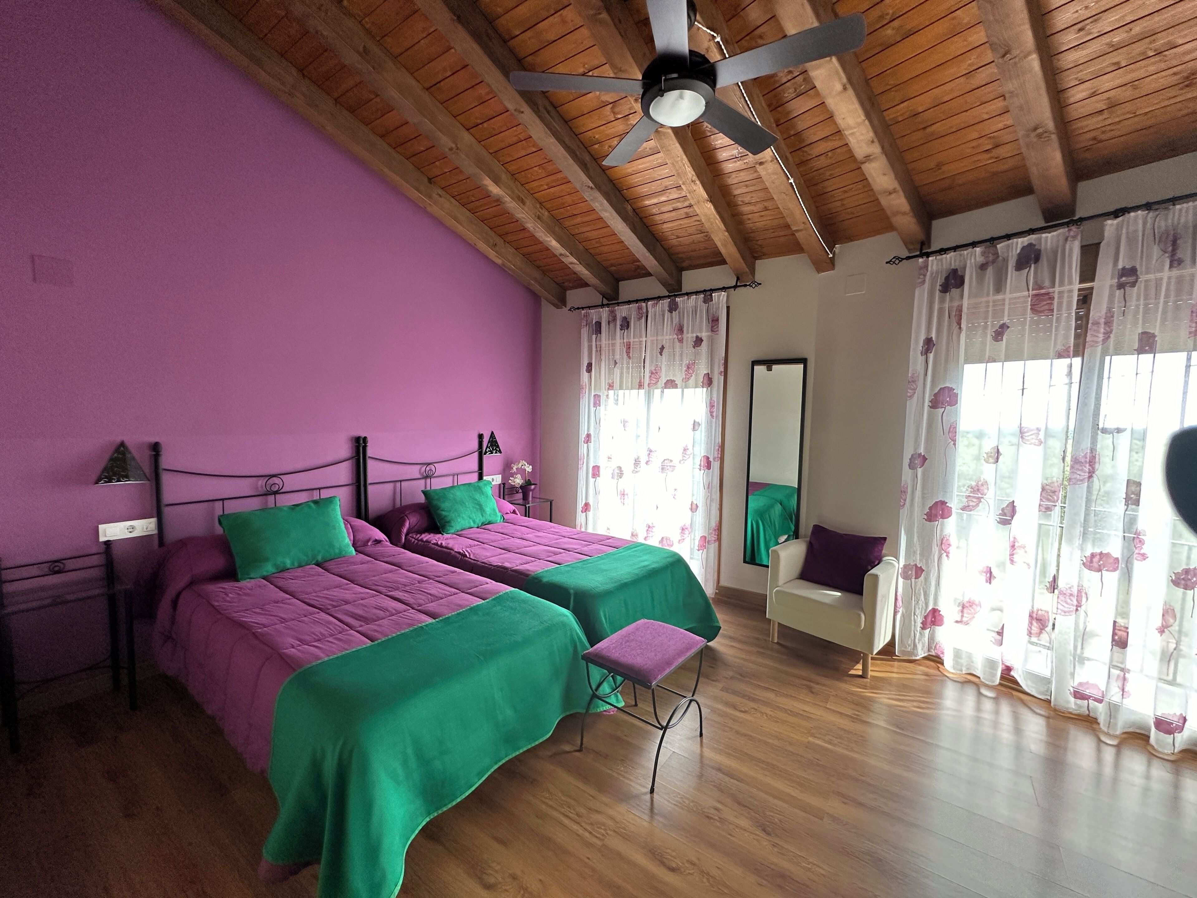 A bedroom with two beds, wooden flooring, a ceiling fan, and floral curtains.