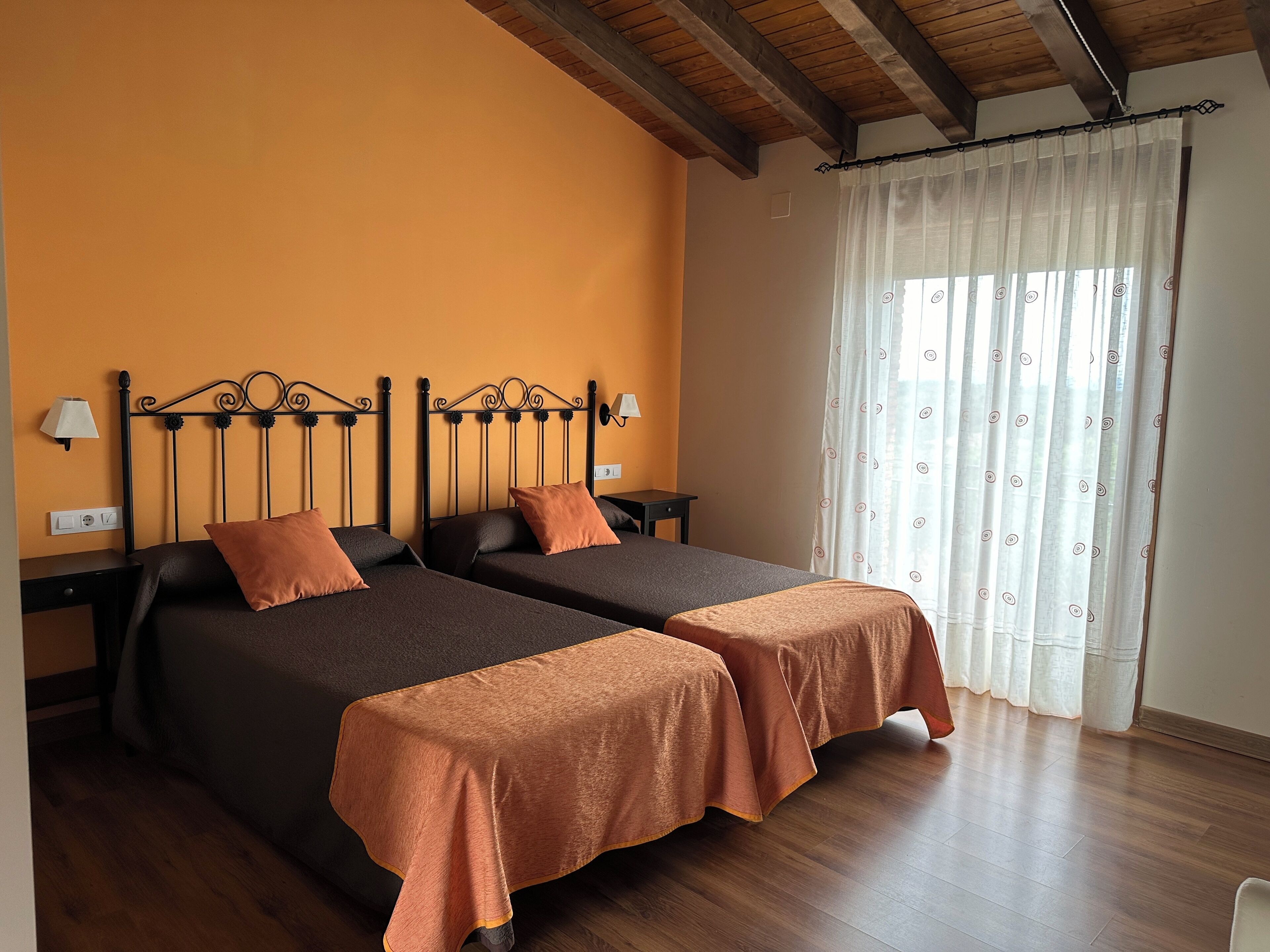 Een kamer met twee bedden, houten vloeren, een raam met gordijnen en een plafond met zichtbare balken.