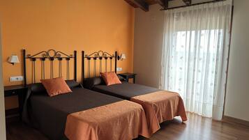 Een kamer met twee bedden, houten vloeren, een raam met gordijnen en een plafond met zichtbare balken.