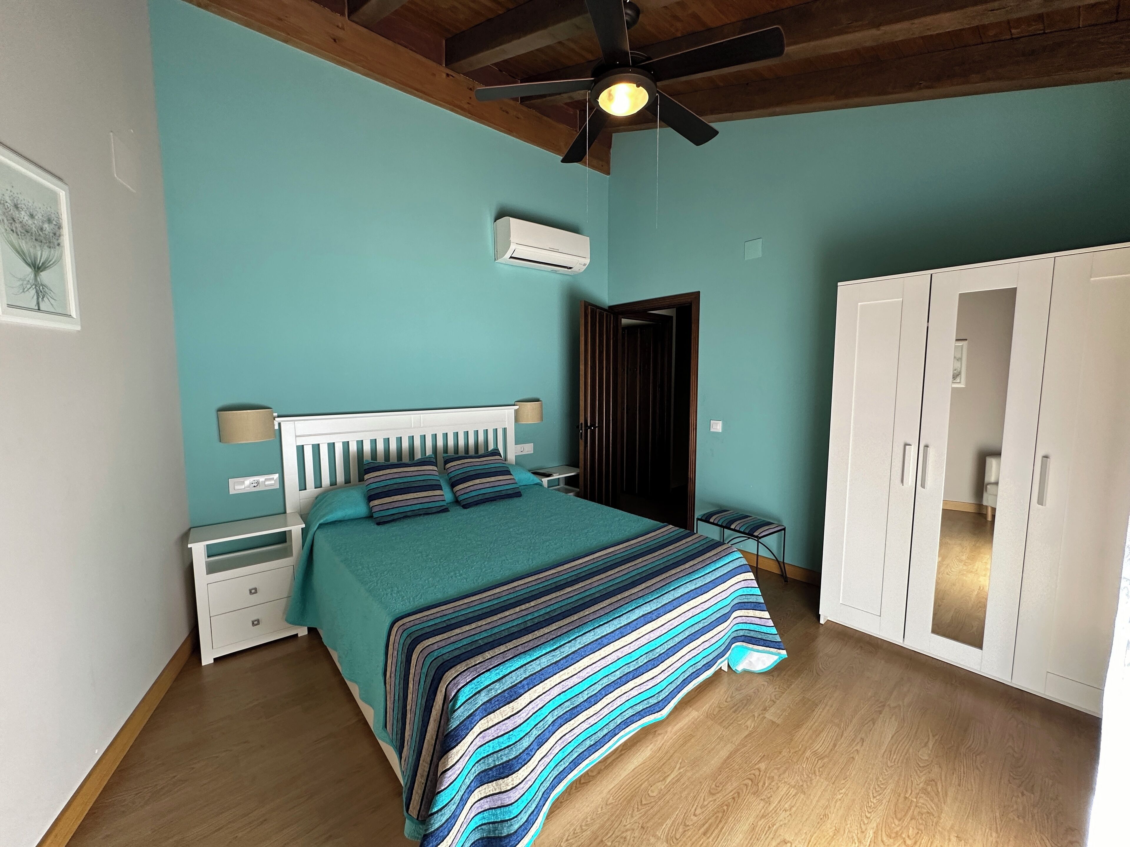 Un dormitorio con cama, mesitas de noche, ventilador de techo, aire acondicionado, armario y una puerta.