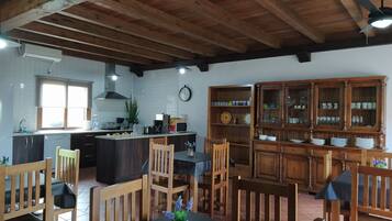 A kitchen with wooden beams, a dining area with wooden chairs, a clock, and a cabinet with dishes.