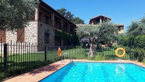 A swimming pool with a stone wall and a metal fence. - Casa Rural La Covacha (Losar de la Vera)